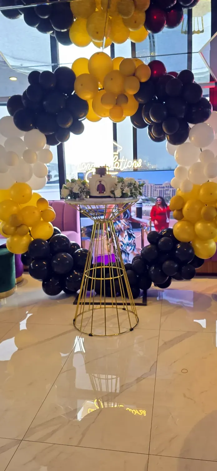 Gold, navy and white balloons around a gold cake stand near tall windows