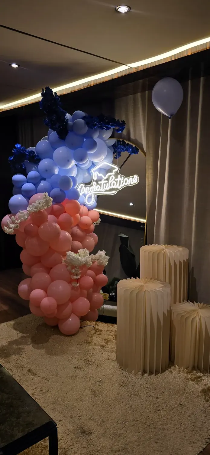 Coral and navy balloon column beside a glowing sign and fluted pillar stands in a dim lounge