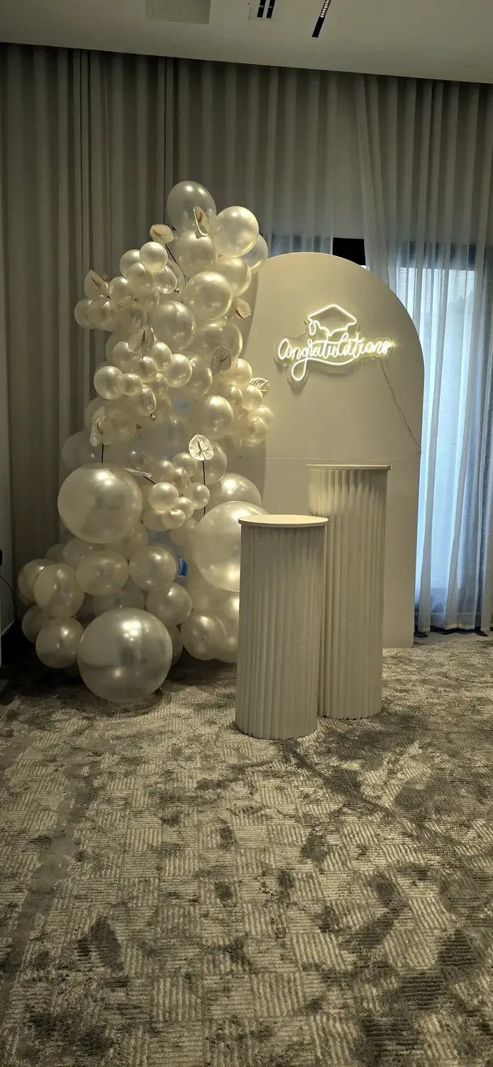 White arch wrapped in pearl and silver balloons, with round plinths on a patterned rug