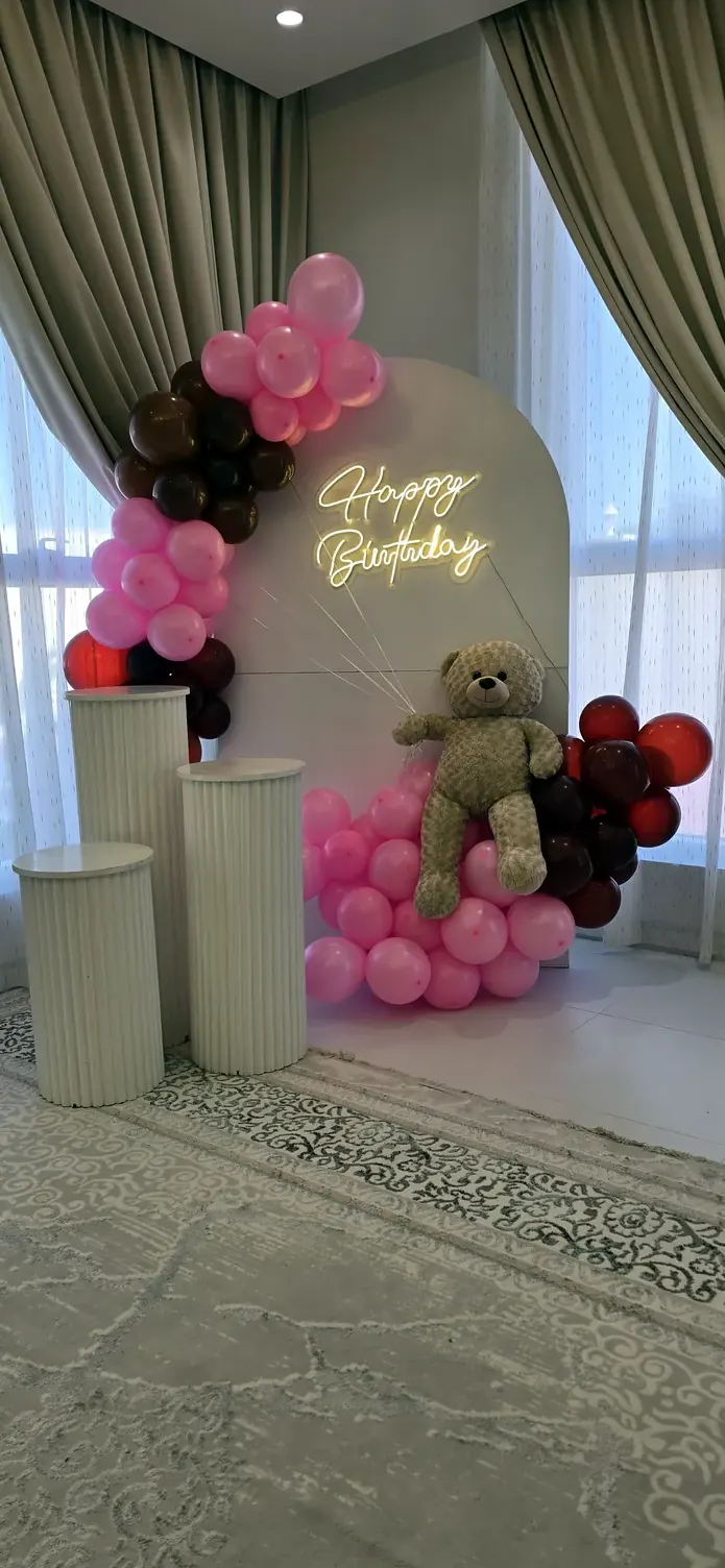 Cream arch with a gold Happy Birthday script, framed by pink, white and burgundy balloons and a teddy bear
